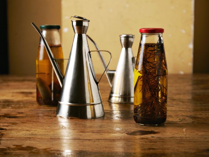 Oil Can Cruet with otgher olive oil jars with herbs on a wood table