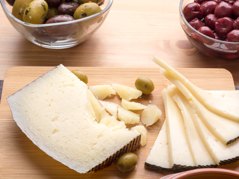 Manchego cheese with olives over a wood board