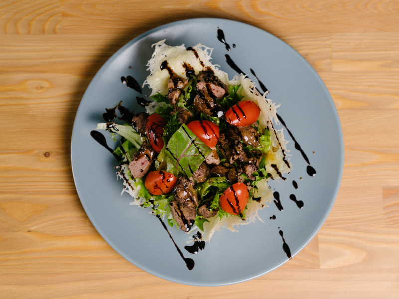 Salad with glaze on a blue plate with a wood background. Deliberico