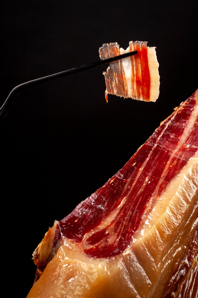 Shiny Iberico ham beautifully cut piece hold by tweezers on black background by Fermin. Deliberico