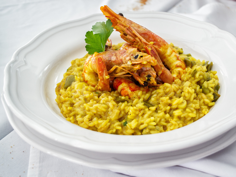 Yellow rice dish topped with prawns and parsley on a white plate and background. Deliberico