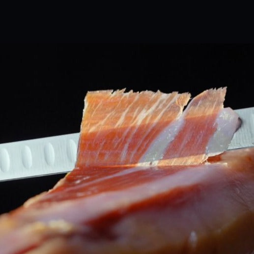 Ham knife cutting ham with a black background by Montaraz. Deliberico