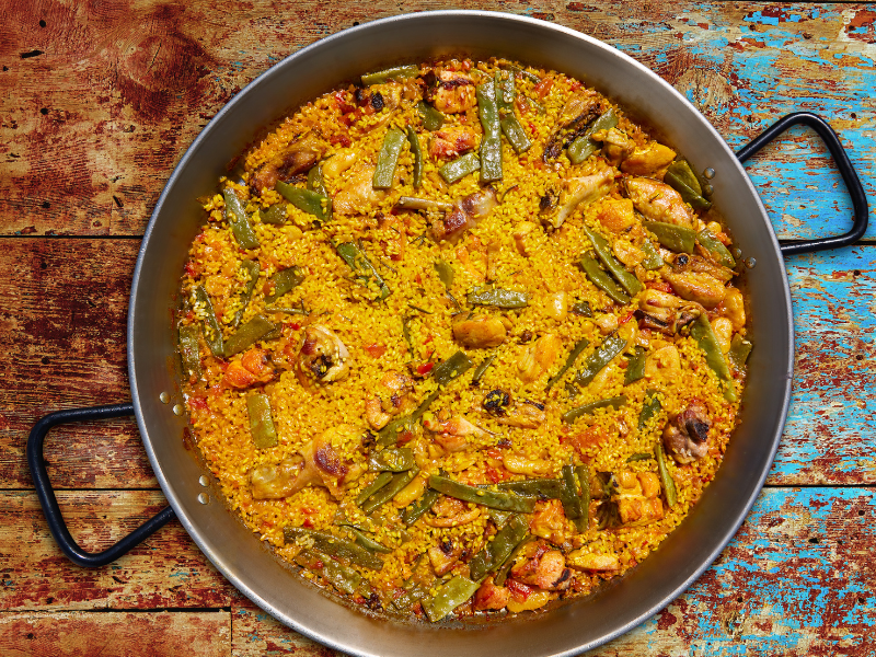 Classic Valencian Paella in a paella pan with a wood background. Deliberico
