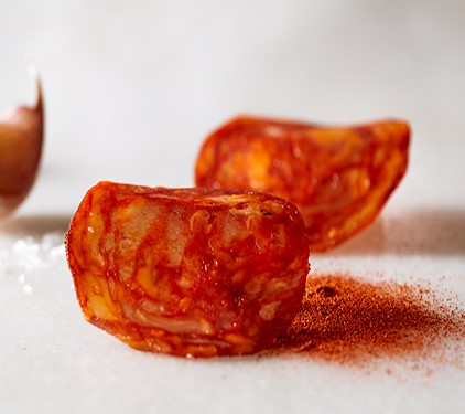 Chorizo thin slices on a marble surface with paprika and salt by Marcos Salamanca. Deliberico