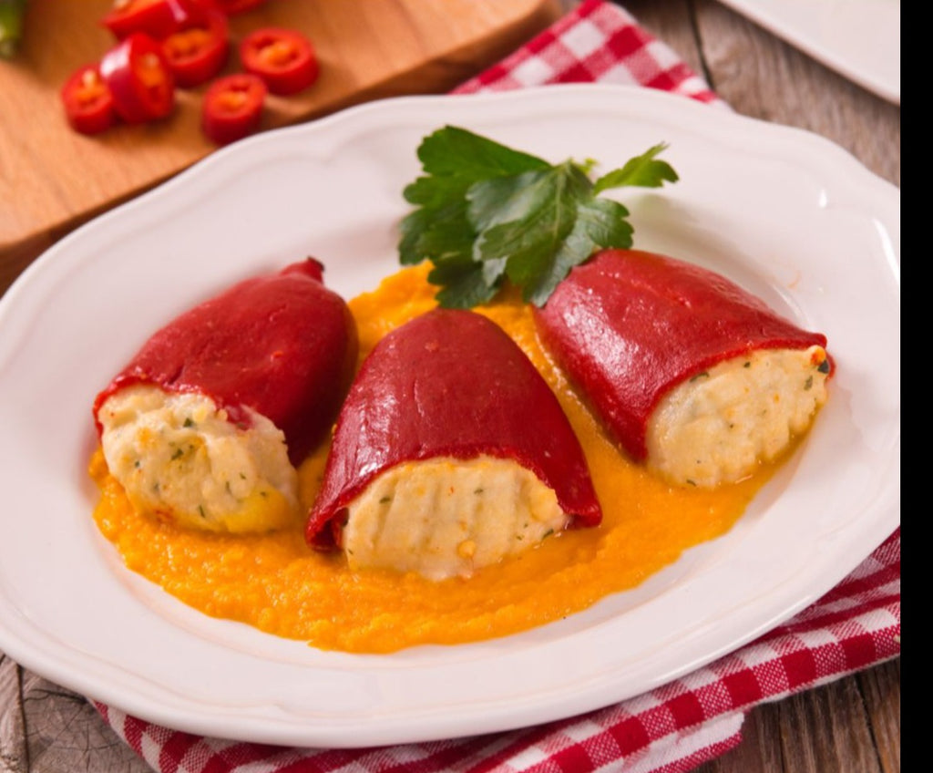 Piquillo peppers stuffed with a creamy sauce and parsley garnish on al round white plate. Deliberico