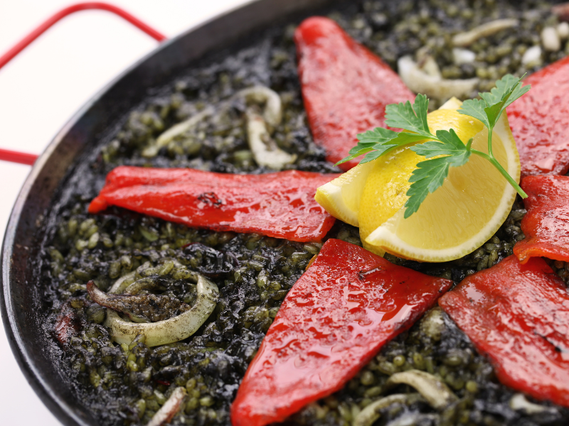 Black Rice pan with cuttlefish decorated with whole piquillo peppers, lemons and parsley. Deliberico