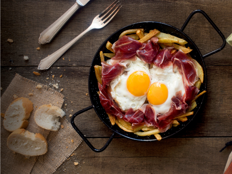 Huevos Rotos with Iberico Ham on black pan on a table