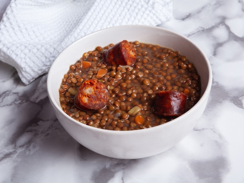 Lentil stew with chorizo iberico in white bowl with marble background