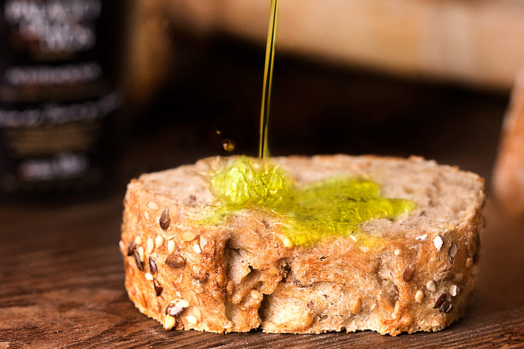 Piece of bread splashed with olive oil over a wood table with the magnun bottle in the back