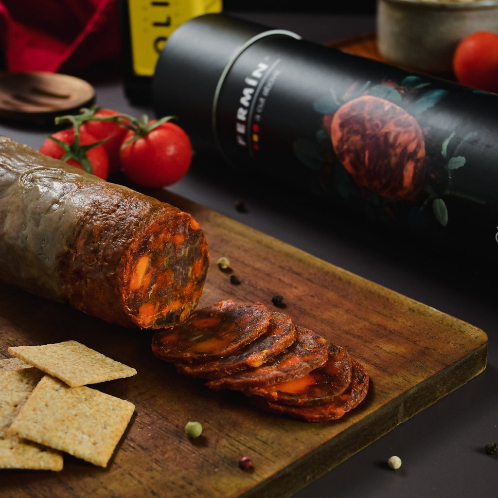 Fermin Iberico Sliced chorizo on a wooden board with crackers and tomatoes, featuring packaging  product in the background