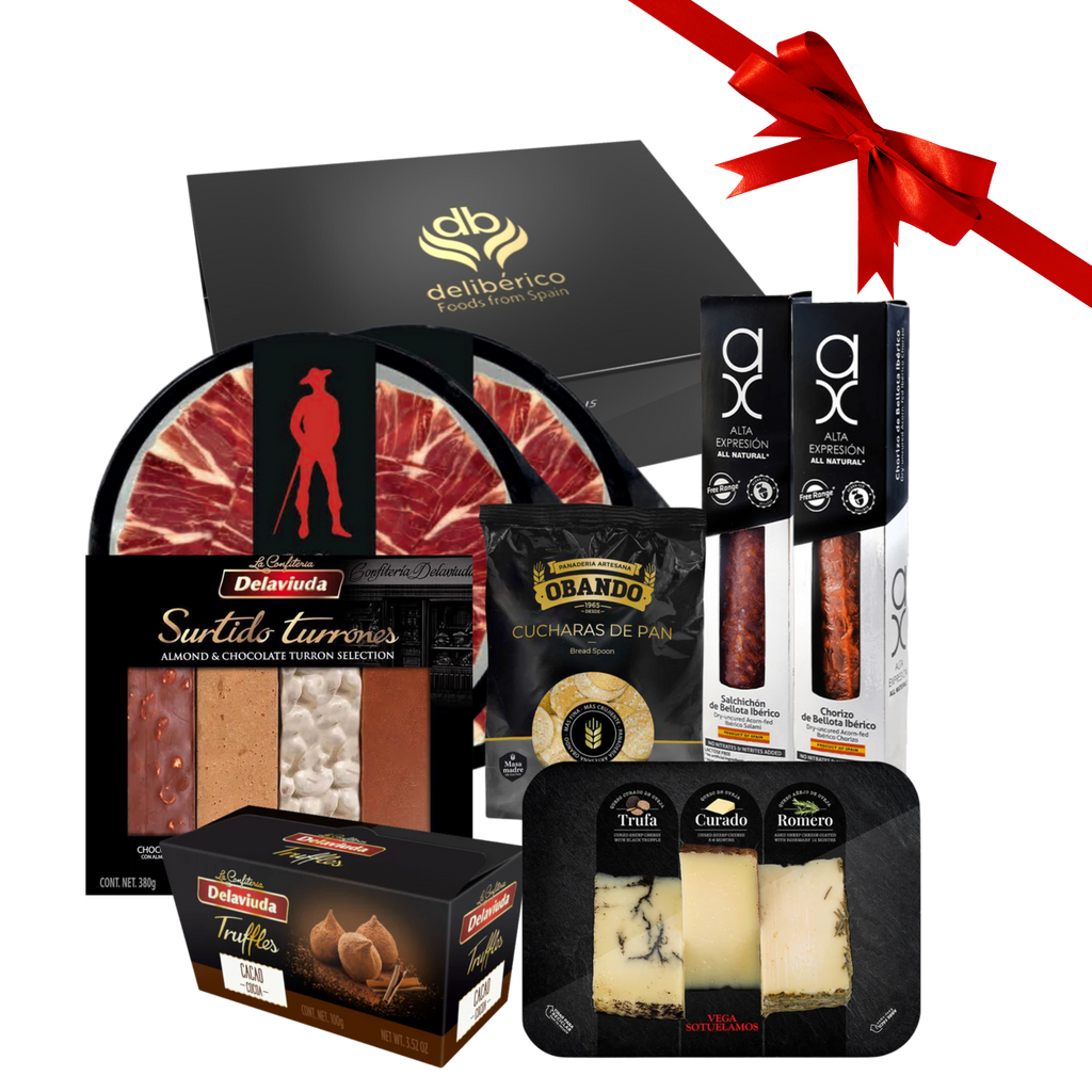 Christmas Time gift box including iberico ham, chorizo and salami, bread spoons, cheese sampler, nougat sampler and cocoa truffles with a red ribbon on a white background
