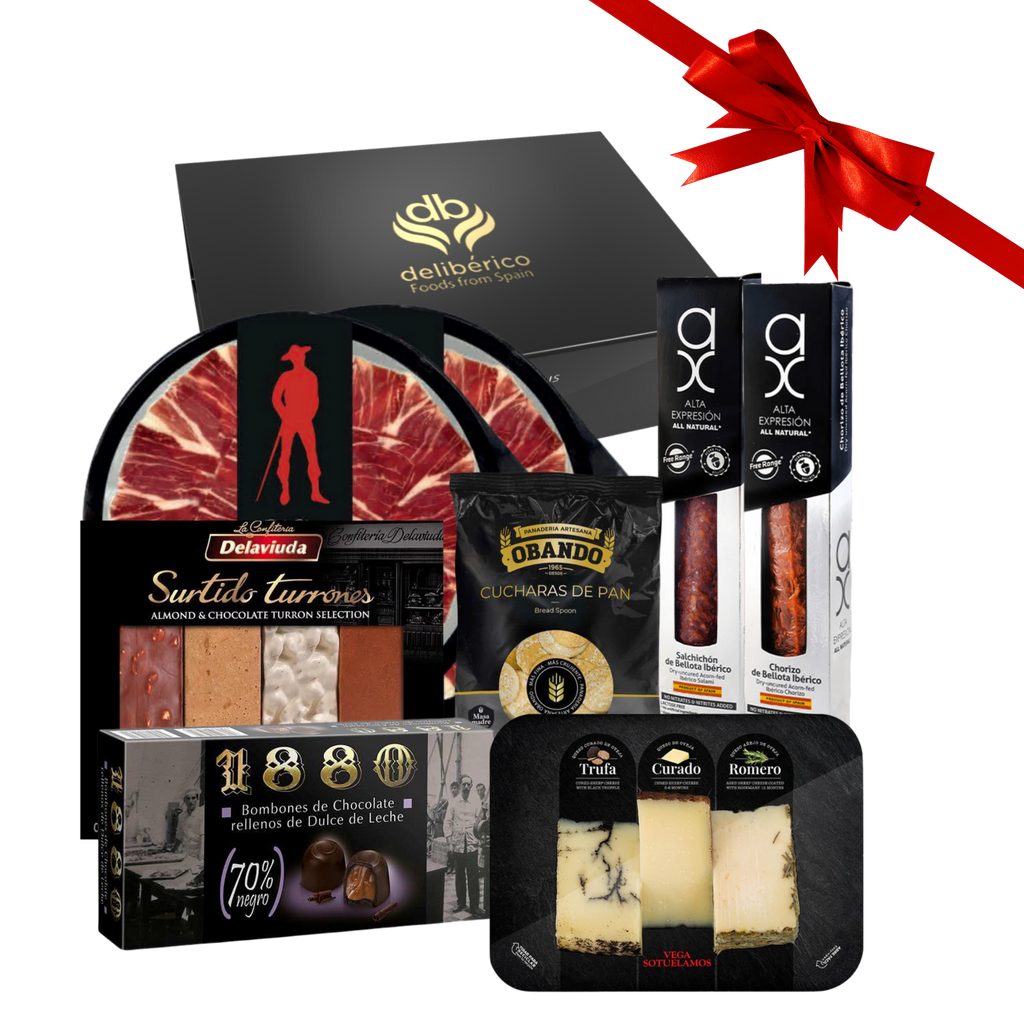 Christmas Time gift box including iberico ham, chorizo and salami, bread spoons, cheese sampler, nougat sampler and dark chocolate bombons with a red ribbon on a white background