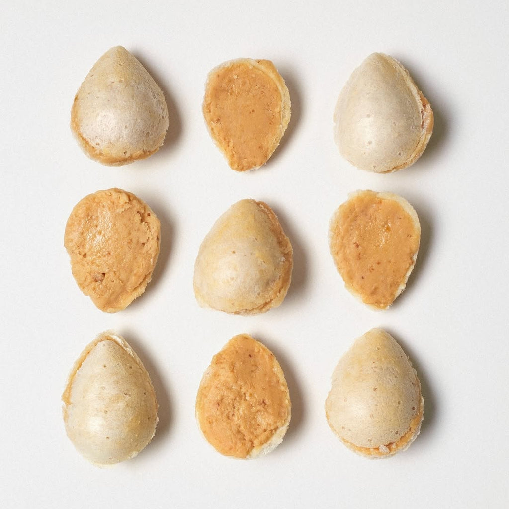 Nine small, almendritas rellenas with a white and brown color pattern on a light gray background