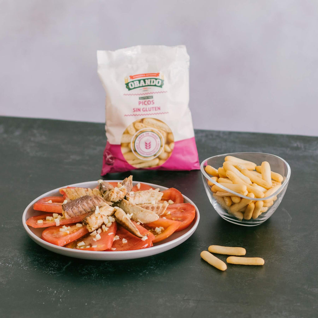 Tuna and tomato plate with gluten free breadsticks by Obando ina a bowl with a pink and white bag over a dark surface
