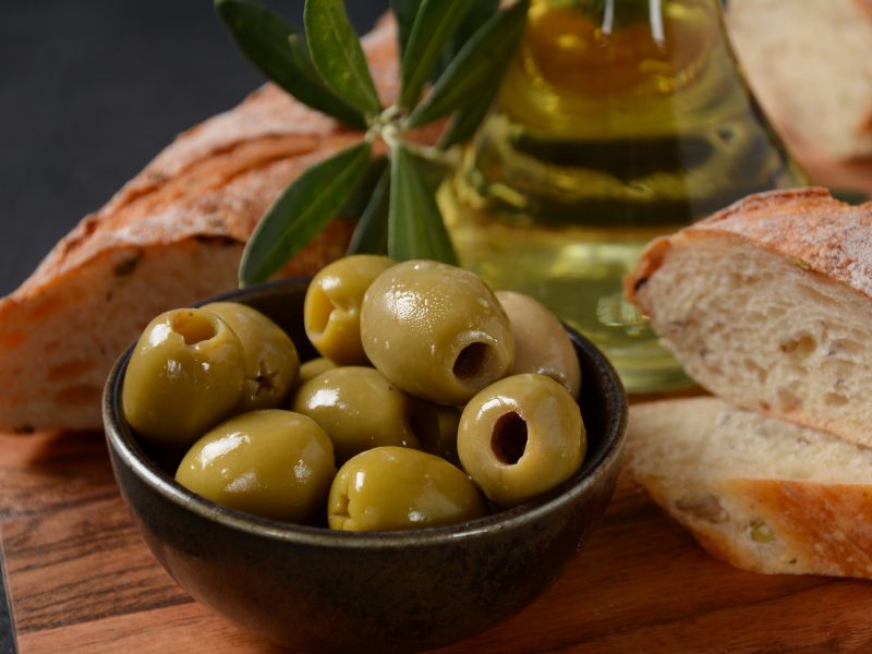 Pitted Gordal  olives in a small bowl next to bread and olive oil