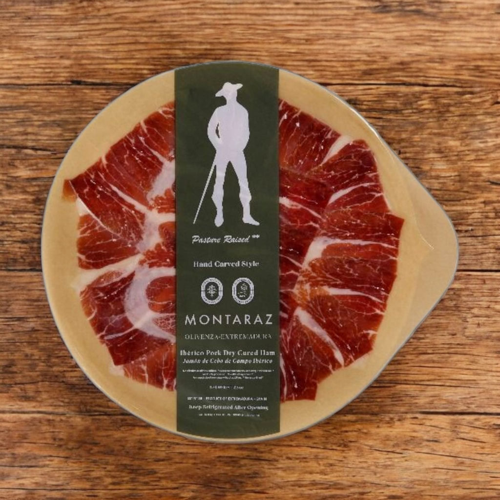 Free Range Iberico pasture-fed Ham Hand Carved Style round packaged plate by Montaraz over wood surface
