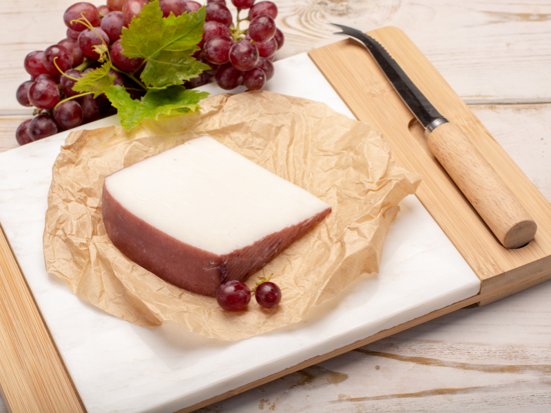The Drunken Goat Queso de Murcia al Vino DOP wedge over a paper and wood board with knife and grapes