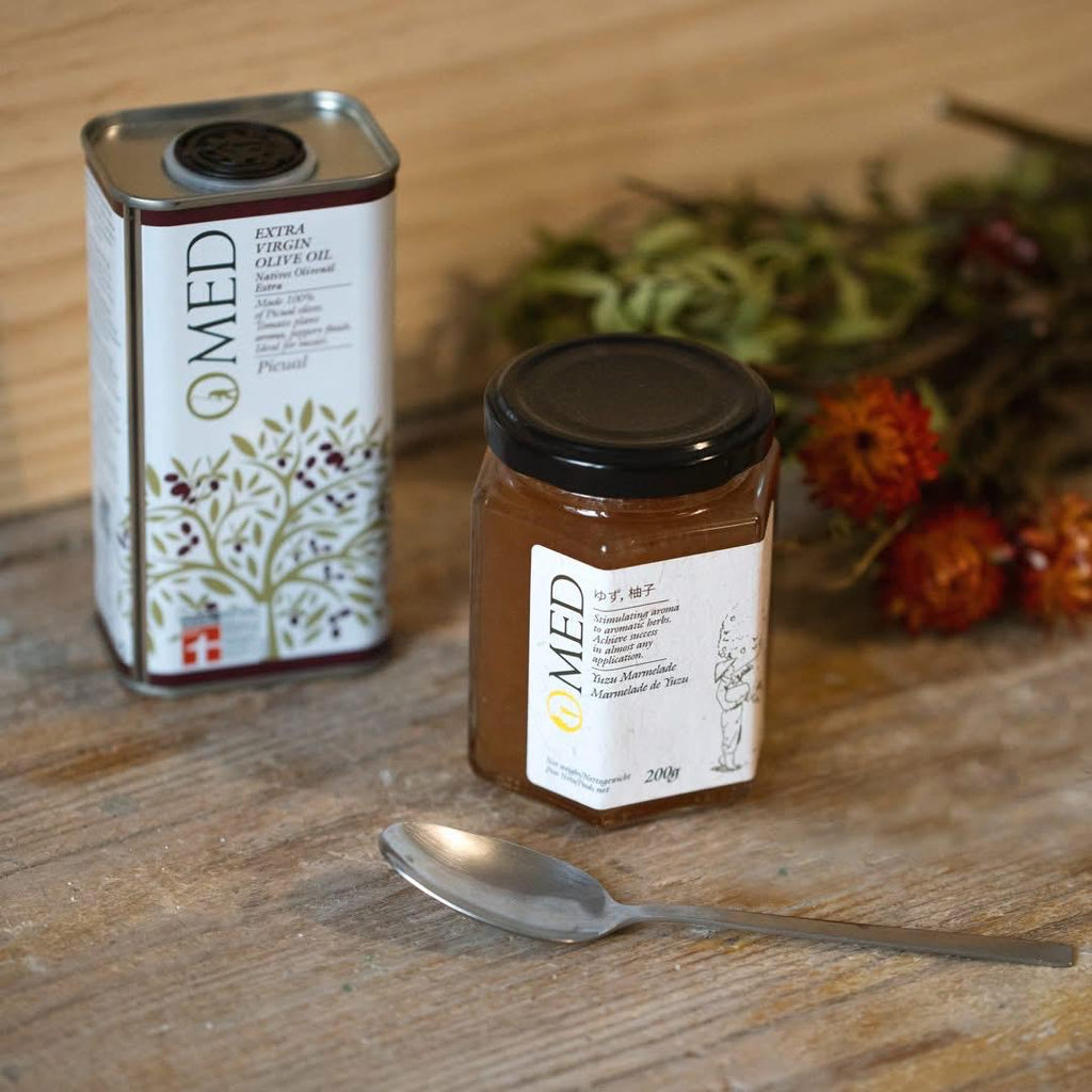 Jar and can of O-med Extra Vigin Olive Oil Picual with a spoon on a wooden surface