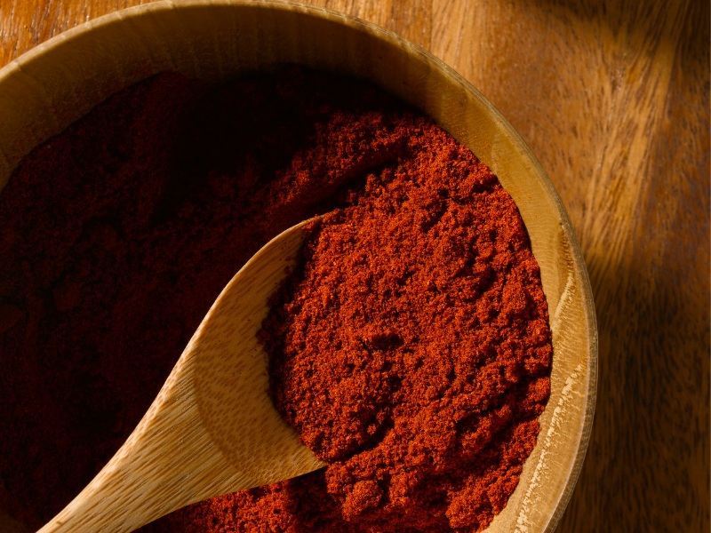 paprika on a wood bowl and wood spoon over a wood surface