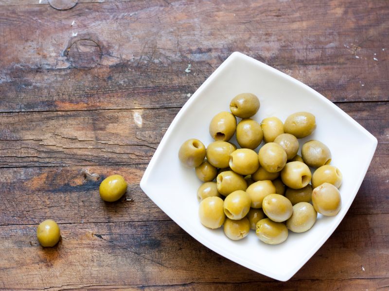 Green manzanilla olives in a white bowl on a wooden surface