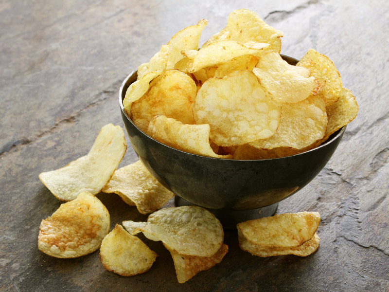 Potato chips in a black bowl over a darl wood table