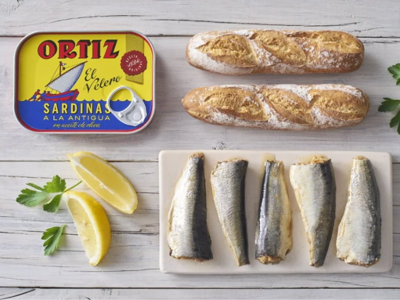 Ortiz can next to bread, a rectangular dish with sardines an lemon wedges and parsley