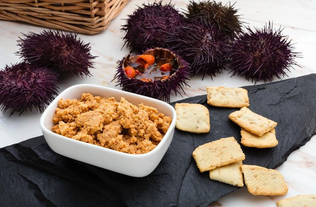 Sea urchin pate scene with pate in a bowl, crackers on a slate and sea urchins on the side