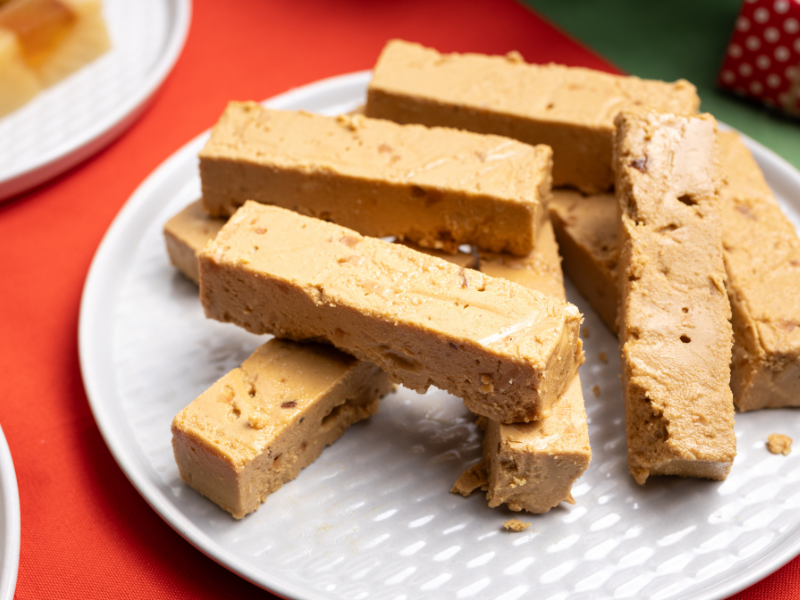 Blocks of brown Jijona nougat Turron on a white plate with a red background