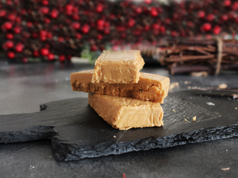 Three pieces of turron Jijona nougat stacked on a black slate surface with a blurred red and brown and red background.