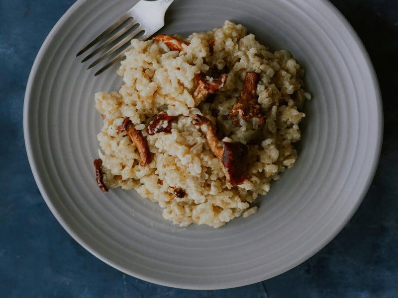 Risotto with mushrooms and rosemary cheese on a white plate with a fork against a blue  background