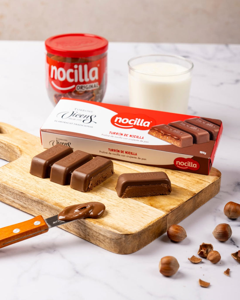 Nocilla chocolate turron by Vicens on a wooden board with a jar of Nocilla and a glass of milk in the background.