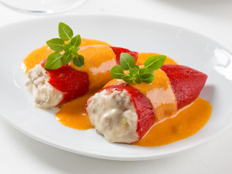 Stuffed piquillo peppers with sauce and green garnish on a white round plate. Deliberico