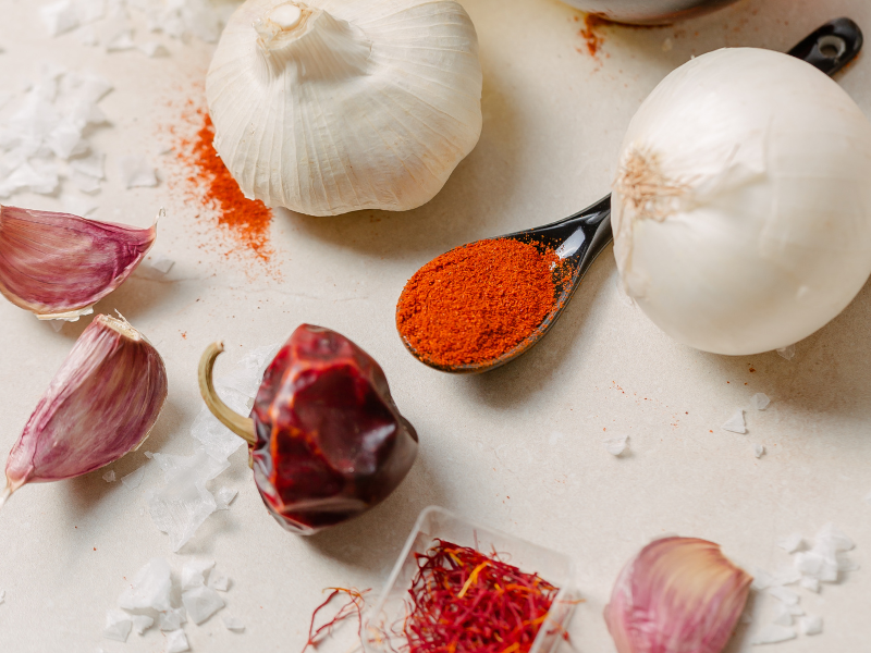 flat lay of spices like ñoras, saffron, paprika, onions, salt and garlic. Deliberico