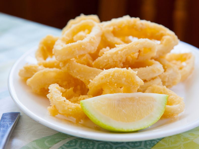 Fried calamari with a lemon wedge on a white plate. Deliberico