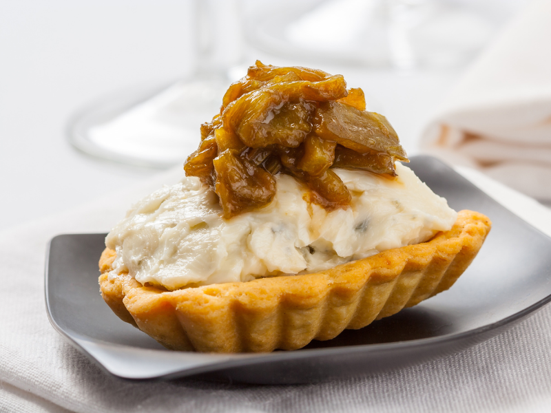 Cabrales appetizer on a shell topped with caramelized onion on a grey plate with a white linen background. Deliberico