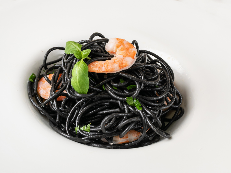 Squid ink pasta dish topped with shrimp and basil. Deliberico 