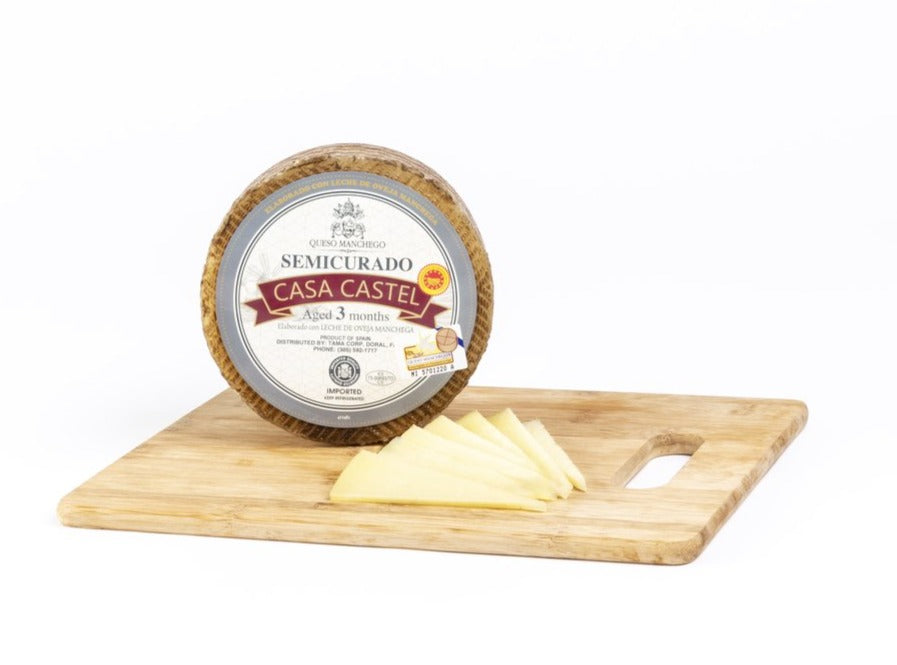 Casa Castel wheel manchego cheese on a wood board with cheese pieces on a side by Deliberico