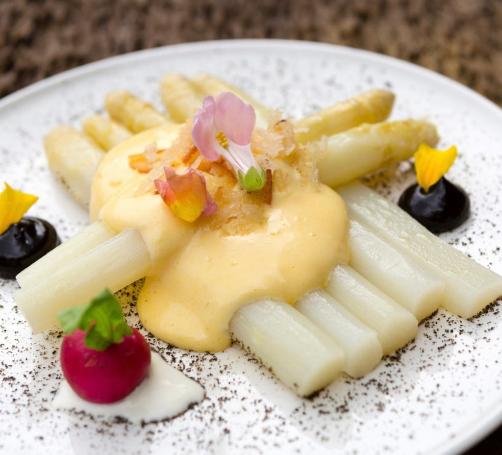 Thick White Asparagus "Cojonudos" with creamy sauce and toppings on white dish by El Navarrico. Deliberico