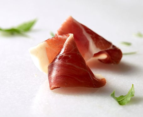 Iberico free range ham sliced by Marcos Salamanca on a marble surface with green garnish. Deliberico