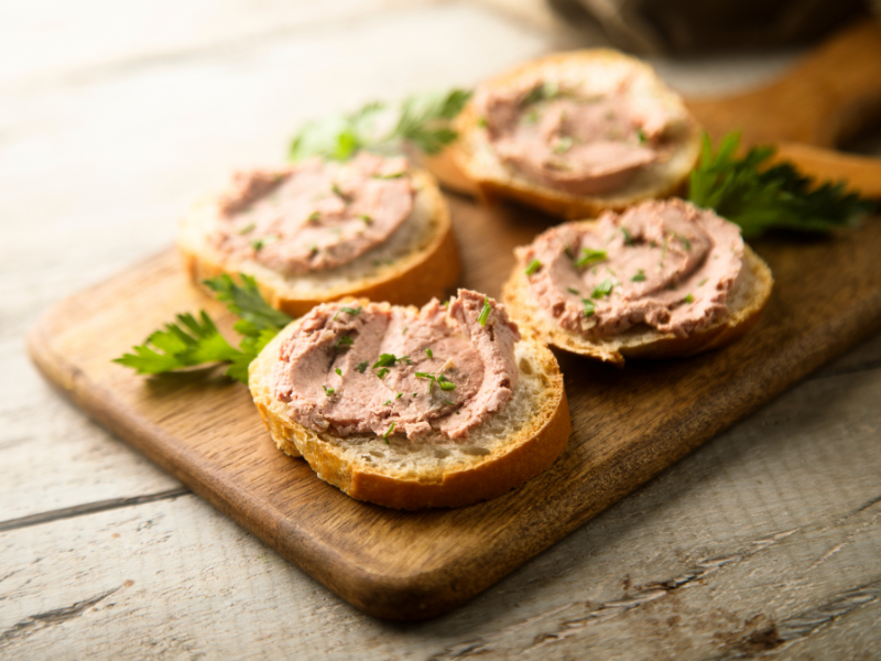 Pate appetizers small round toast on a wood board with parsley garnish. Deliberico
