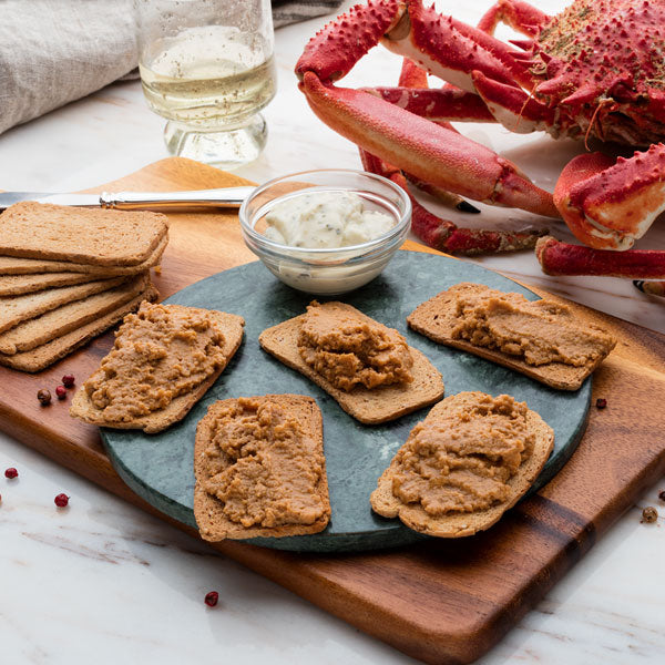 Lobster pate on crackers over round slate and wood board next to white and spider crab. Deliberico