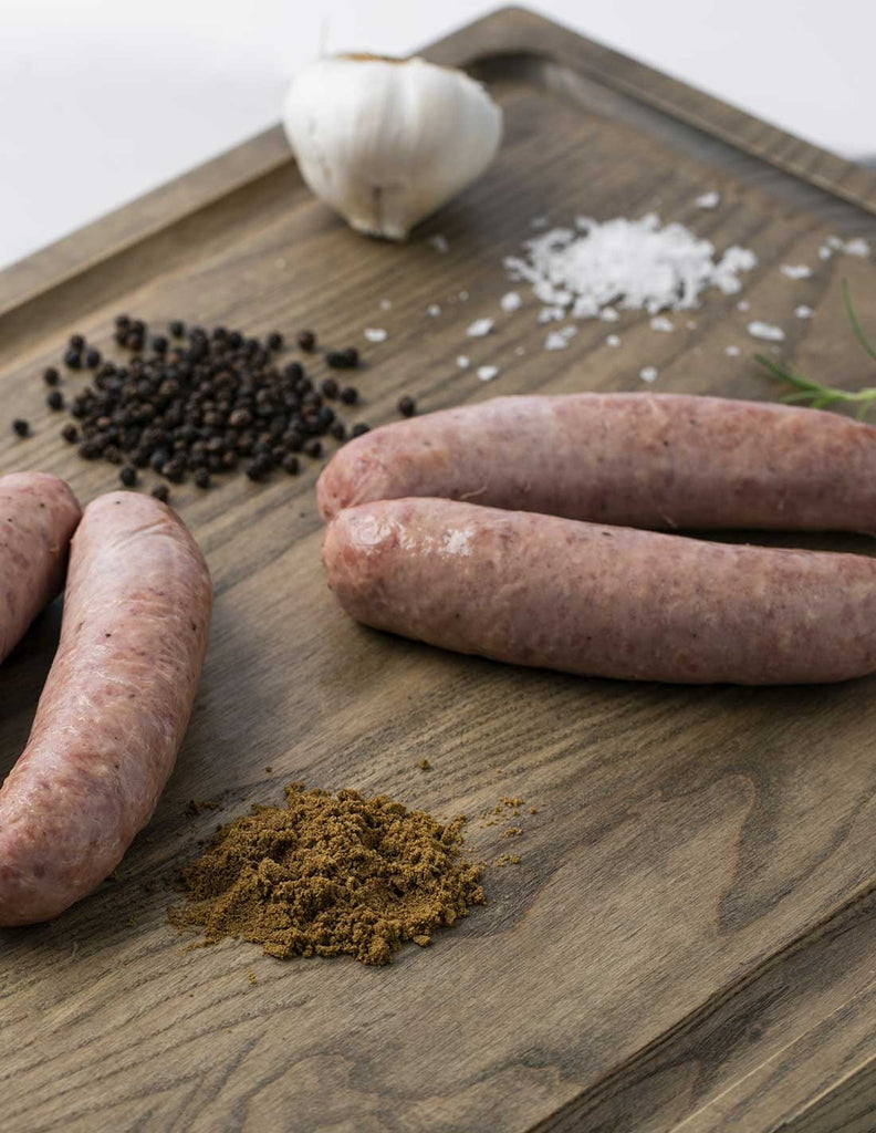 Butifarra white sausage on a wood board with spices like black pepper, salt, garlic by Dona Juana. Deliberico