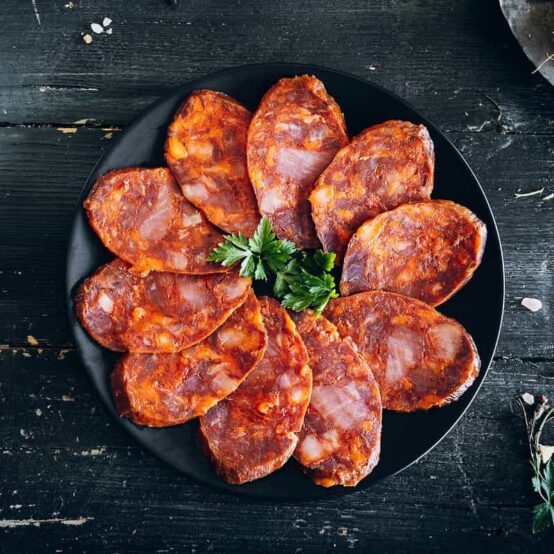 100% Ibérico Acorn-fed chorizo sliced on black round plate with parsley in center by COVAP. Deliberico