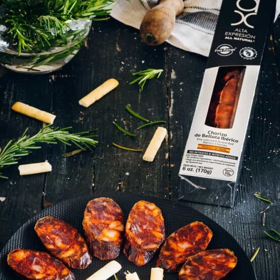 All Natural 100% Iberico Acorn-Fed chorizo in black plate with  rosemary and breadticks and black and silver box by COVAP. Deliberico